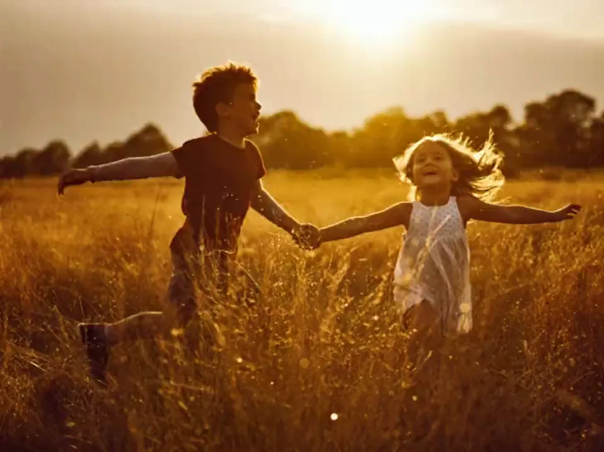 Two kids running hand-in-hand through golden grass at sunset