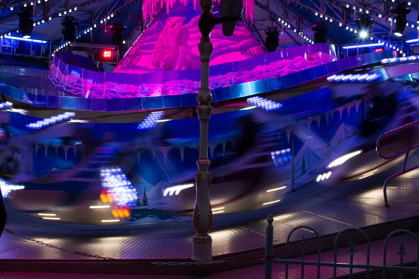 Spinning fairground ride under purple and blue lights at night, before the preset